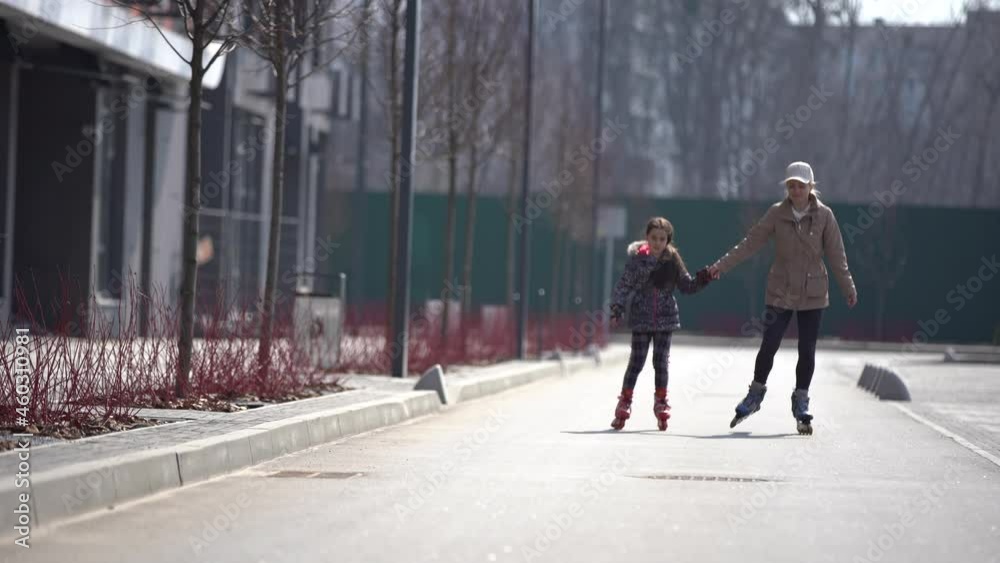Mother Teaching Daughter Roller Skating in the City Park in Slow Motion. Rear View. Family Sport Activities Outdoors. People, Children, Childhood Concept. Mother Teaching Daughter Roller Skating in the City Park in Slow Motion. Rear View. Family Sport Activities Outdoors. People, Children, Childhood Concept.