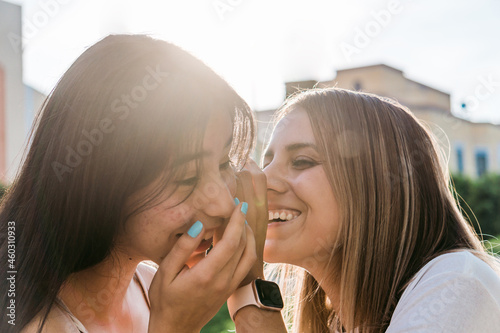 Smiling teenager telling secret to girlfriend on street photo