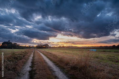 Dirt road through the field and clouds after sunset