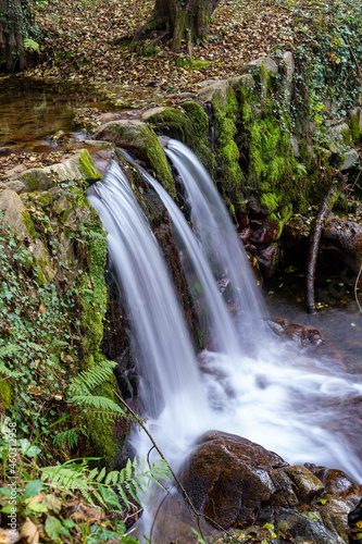 small waterfall falling down stone wall with autumnal leaves, manlleu catalonia, spain