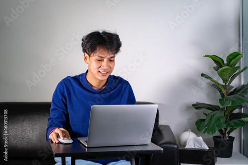 young man using laptop computer, typing on keyboard, writing email or message, chatting, shopping, lerning, successful freelancer working online on computer, sitting in modern living room at home.