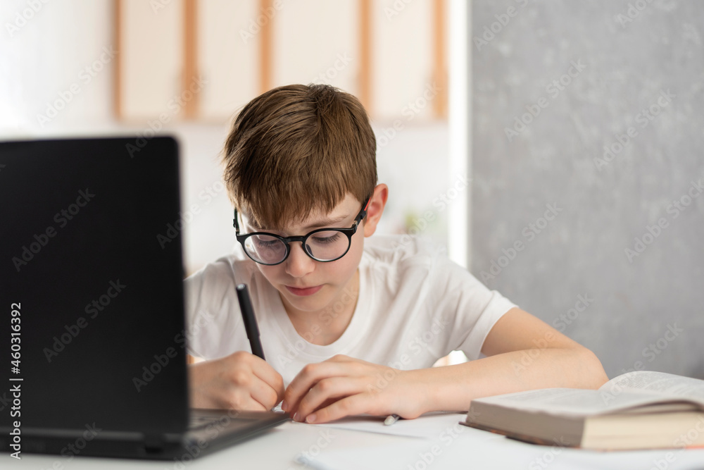 Child at home near laptop during distance learning. Online lessons. Teen boy does homework at computer. Home schooling Child at home near laptop during distance learning. Online lessons. Teen boy does homework at computer. Home schooling