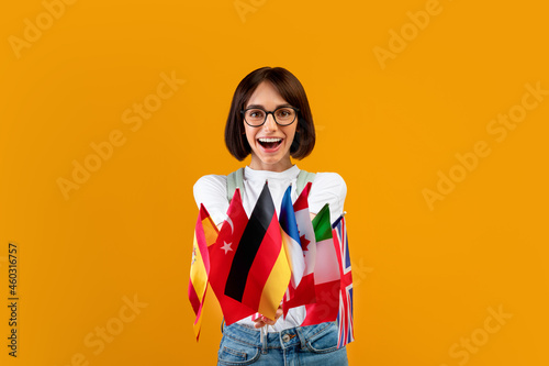 Foreign language studying school concept. Excited lady showing bunch of diverse flags, posing over yellow background photo