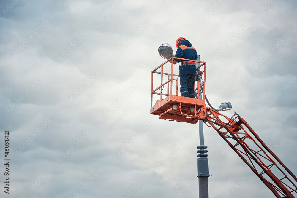 Street light repair works, worker repair street lamp at height, led lights replacement. Man in lift bucket wearing personal protective equipment fix light pole lamp.