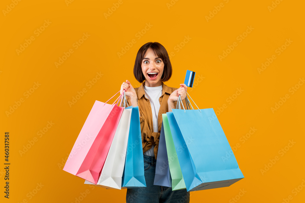 Sales and discounts concept. Excited woman holding credit card and colorful shopping bags, yellow background