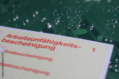 Viersen, Germany - May 9. 2021: Yellow certificate of work incapacity (german: Arbeitsunfähigkeitsbescheinigung) on green computer circuit board