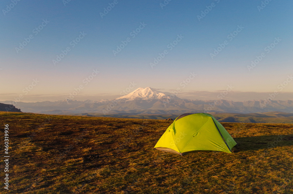 Camping on Bolshoy Bermamyt Plateau lit by sunrise. Scenic view of two summits of Mt Elbrus in background. Mt Elbrus - highest and most prominent peak in Russia and Europe. Russia, Karachay-Cherkessia