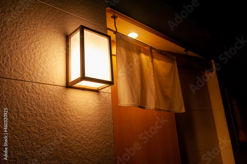 小料理居酒屋の入り口の暖簾と、光が灯る看板 