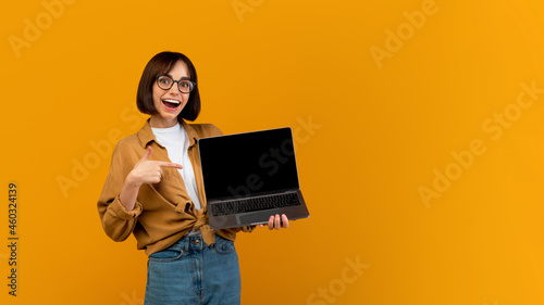 Wow, great website. Excited lady pointing at laptop with black screen, standing over yellow background, free space