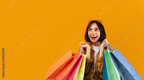 Excited lady with shopping bags smiling and looking at free space, offering place for your ad over yellow background