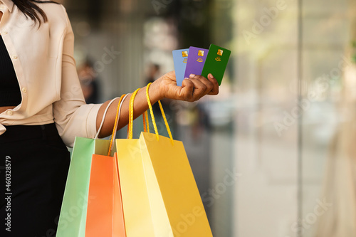 Unrecognizable black woman holding three credit cards and shopping bags