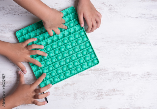 Child with green poppit game. Close up bunner shot of kid hands playing with green pop It fidget toy photo