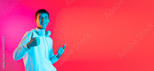 Flyer with young man, student or boy in casual clothes smiling isolated on magenta studio backgroud in neon. Human emotions concept.