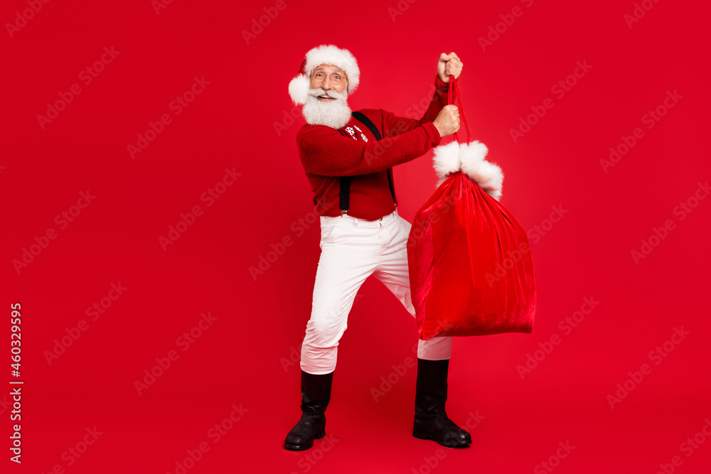 Full length photo of santa claus happy positive smile hold bag present newyear isolated over red color background Full length photo of santa claus happy positive smile hold bag present newyear isolated over red color background
