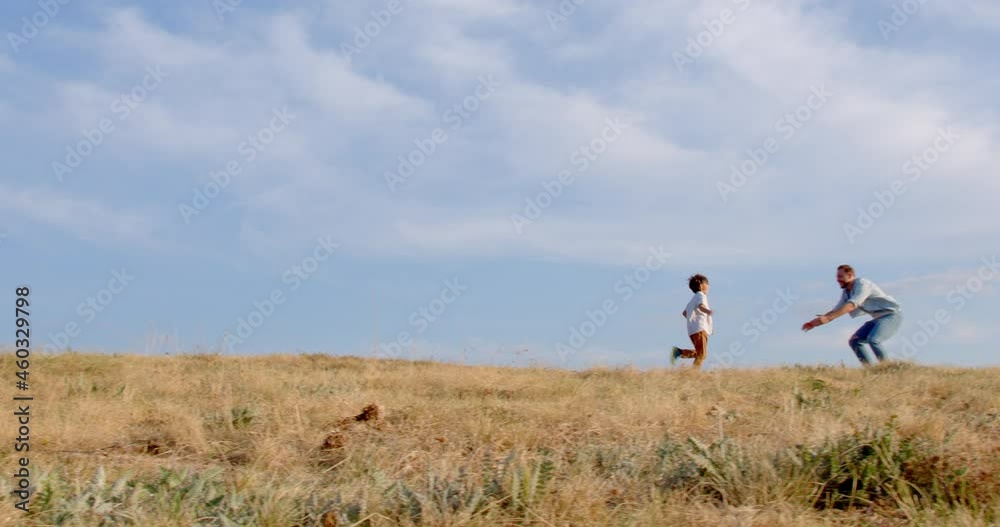 A boy runs across yellow field towards his father arms against blue sky. Happy father takes his son in his arms and turns him. Father, son play together, strong friendship father and son. A boy runs across yellow field towards his father arms against blue sky. Happy father takes his son in his arms and turns him. Father, son play together, strong friendship father and son.