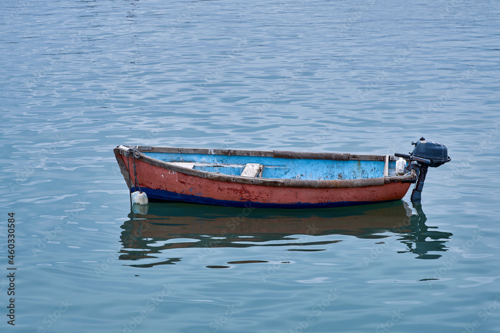 Small wooden fishing boat with one outboard motor in clear blue water.