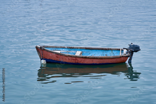 Small wooden fishing boat with one outboard motor in clear blue water. photo