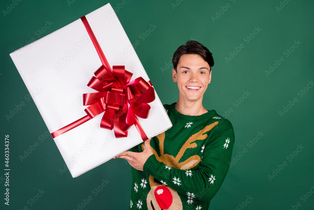 Photo of nice positive guy hold big large present box wear deer ornament sweater isolated green color background Photo of nice positive guy hold big large present box wear deer ornament sweater isolated green color background
