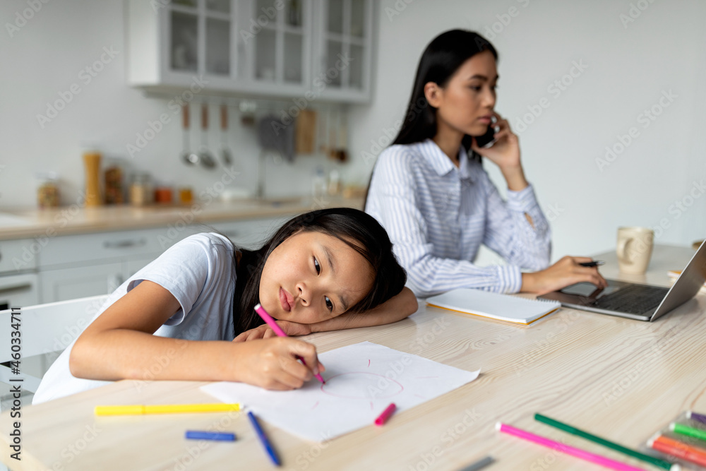 Boredom concept. Busy mom working remotely at home and ignoring her little daughter, kid feeling bored and lonely Boredom concept. Busy mom working remotely at home and ignoring her little daughter, kid feeling bored and lonely