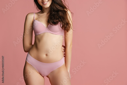 Cropped image of young beautiful slim woman in lingerie posing isolated over pink studio background. Natural beauty concept.