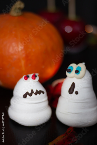 Engaging duo of meringue specters  one startled and the other perturbed  stand proudly beside a fresh Halloween pumpkin.