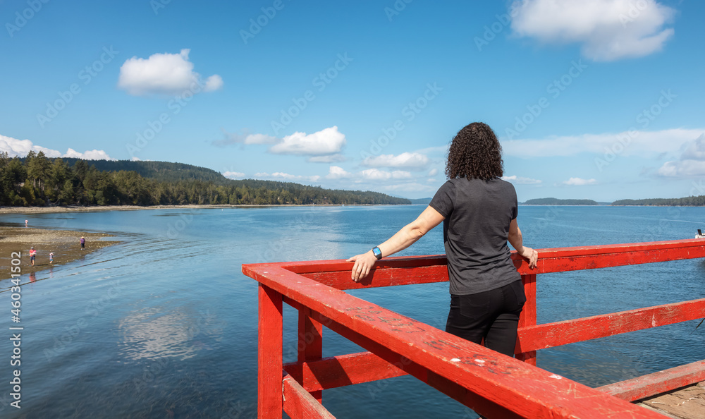 White Caucasian Woman on a Wooden Pier by the Pacific Ocean West Coast. Sunny Summer Day. Fernwood Point Beach, Salt Spring Island, British Columbia, Canada. White Caucasian Woman on a Wooden Pier by the Pacific Ocean West Coast. Sunny Summer Day. Fernwood Point Beach, Salt Spring Island, British Columbia, Canada.