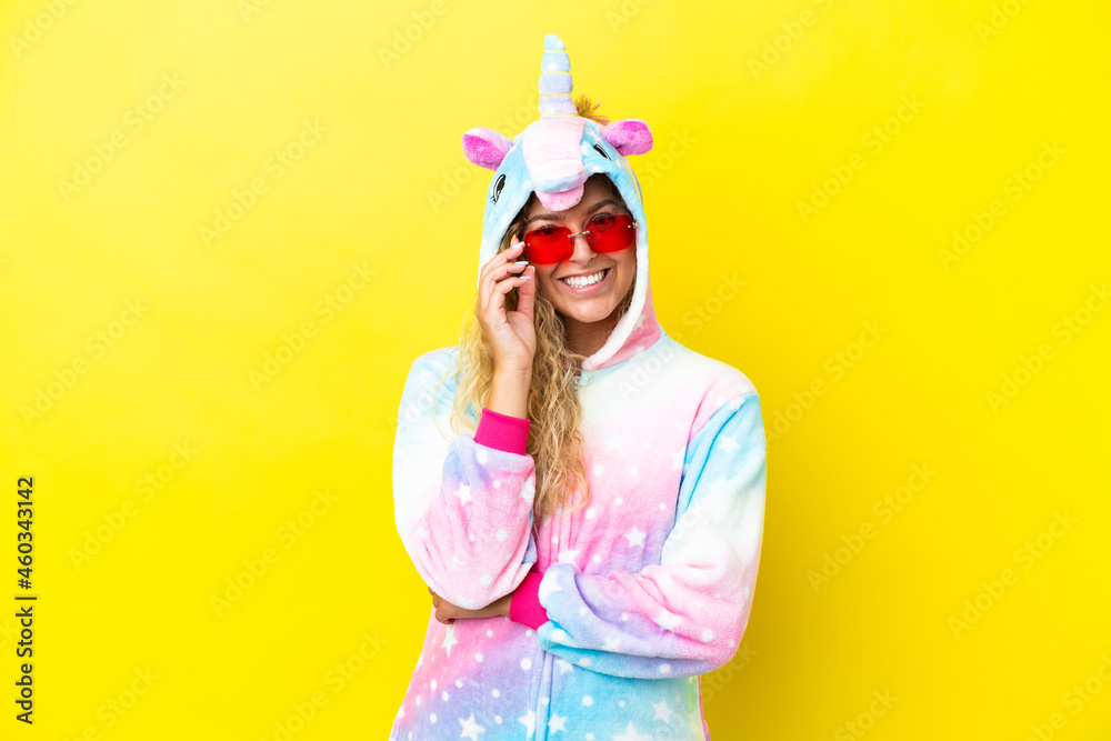 Girl with curly hair wearing a unicorn pajama isolated on yellow background with glasses and happy Girl with curly hair wearing a unicorn pajama isolated on yellow background with glasses and happy