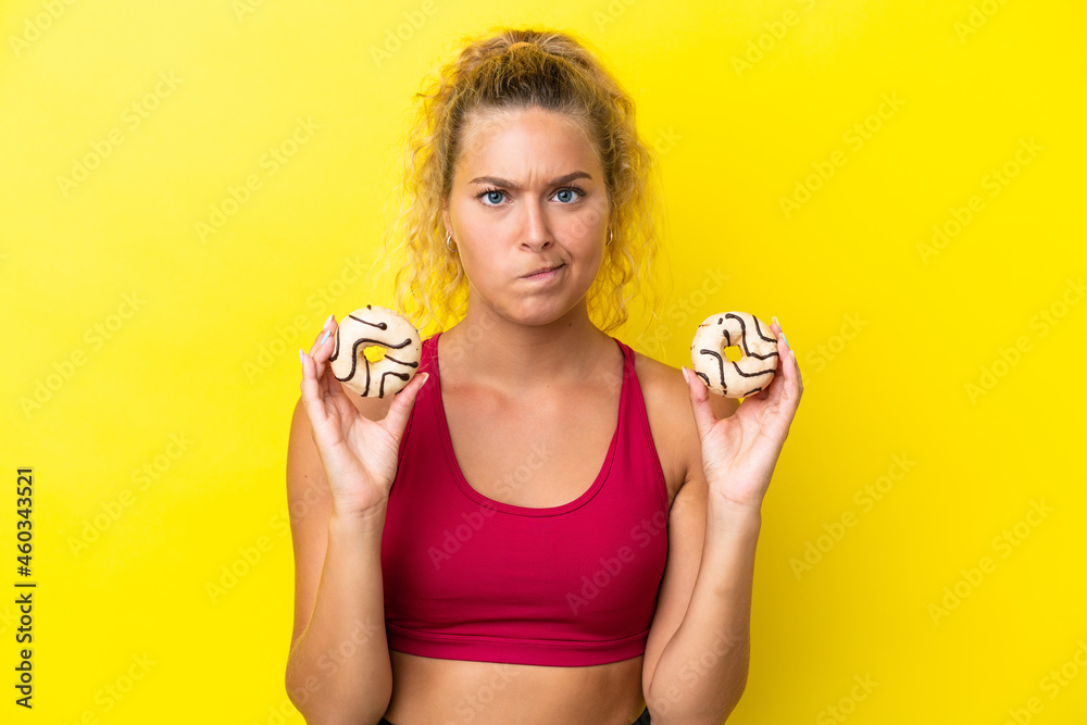 Girl with curly hair isolated on yellow background holding donuts with sad expression Girl with curly hair isolated on yellow background holding donuts with sad expression