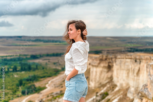 Portrait of a beautiful young woman in a white shirt on the edge of a cliff with an endless panorama, White Rock in the Crimea. The concept of travel © KseniaJoyg