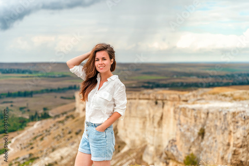 Portrait of a beautiful young woman in a white shirt on the edge of a cliff with an endless panorama, White Rock in the Crimea. The concept of travel