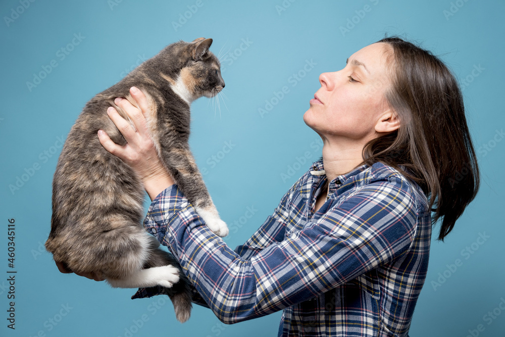 Woman in a shirt holds her adorable cat in her hands and looks at her attentively. Concept of playing and taking care of pets. 