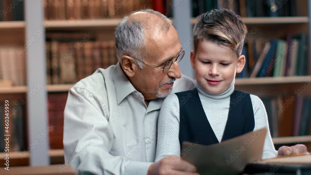 Happy old man grandfather and kid grandson learning antique historical paper documents at library Happy old man grandfather and kid grandson learning antique historical paper documents at library