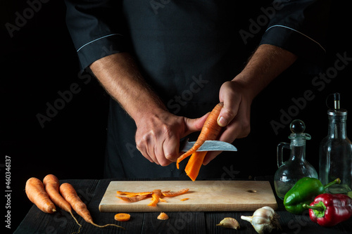 Chef peels carrots for vegetable soup in a restaurant kitchen. Close-up - hands of the cook during work. Carrot diet