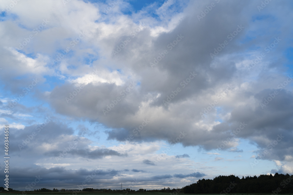 View of the beautiful, autumn, blue sky with textured gray clouds. In the background, you can see a forest and a power line support. Landscape.