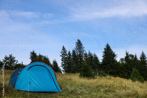 Blue camping tent on green grass near forest, space for text