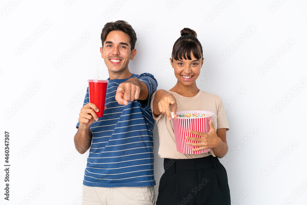 Young mixed race friends isolated on white background holding a big bucket of popcorns while pointing front