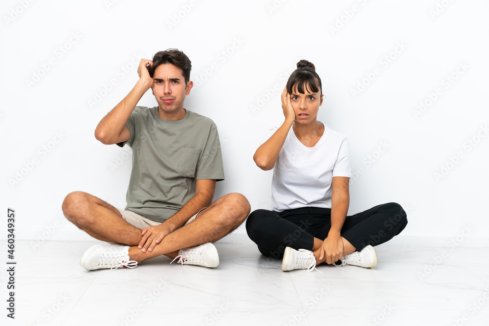 Young mixed race couple sitting on the floor isolated on white background with an expression of frustration and not understanding Young mixed race couple sitting on the floor isolated on white background with an expression of frustration and not understanding
