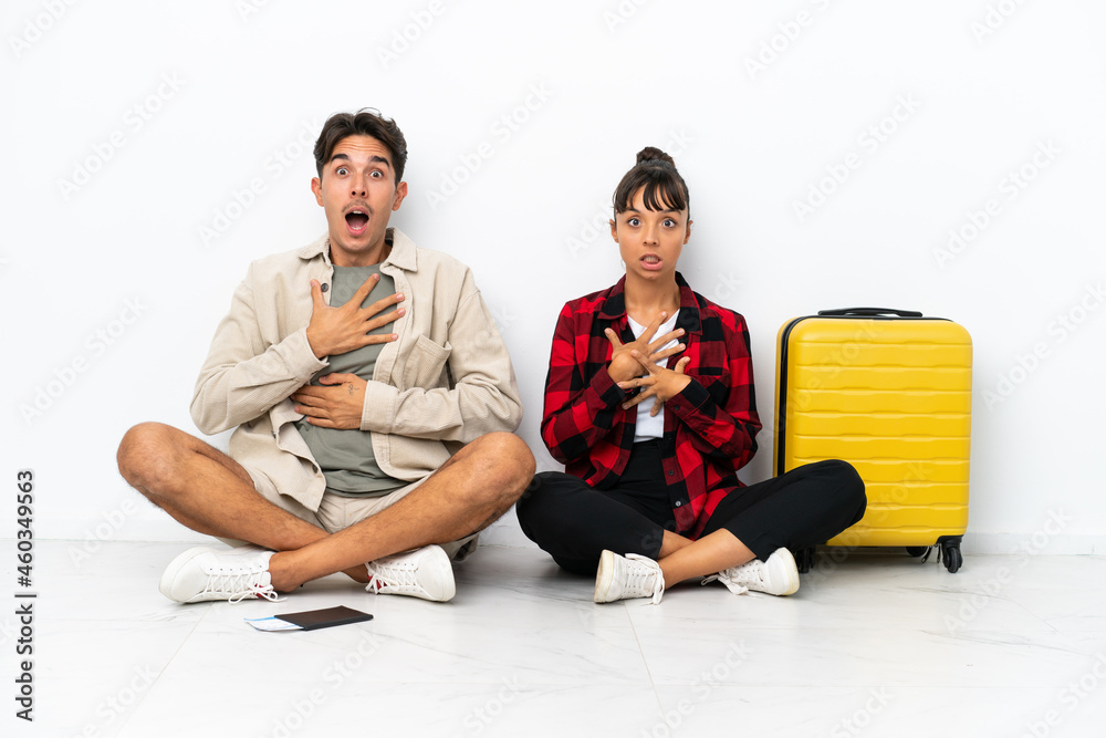 Obraz premium Young mixed race travelers couple sitting on the floor isolated on white background surprised and shocked while looking right