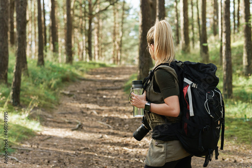 Female hiker with big backpack and reusable bottle for water in green forest photo