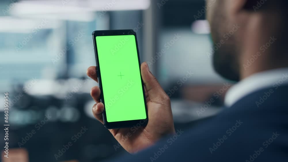 Black Businessman with Green Screen Chroma Key Smartphone in Office. African-American Businessperson using Internet, Social Media, Online Shopping with Mobile Phone Device. Over Shoulder