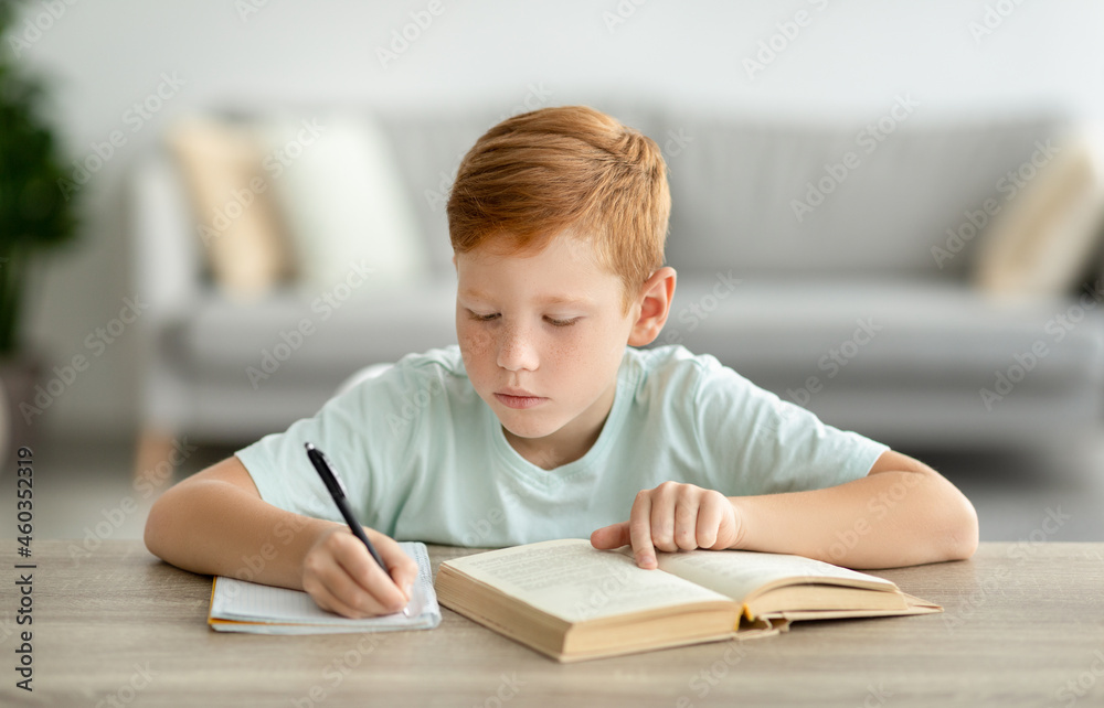 Smart redhead boy reading book and taking notes Smart redhead boy reading book and taking notes