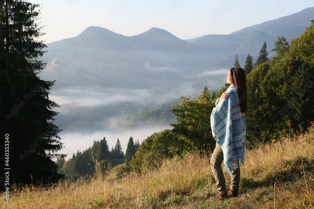 Woman with cozy plaid enjoying warm sunlight in mountains