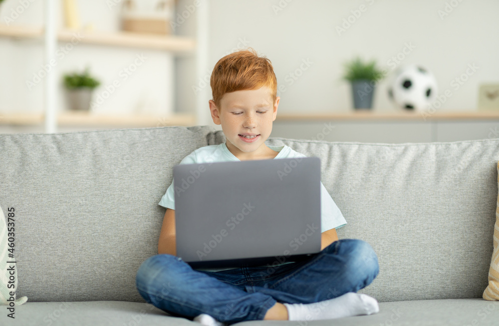 Redhead child using laptop, playing online video game