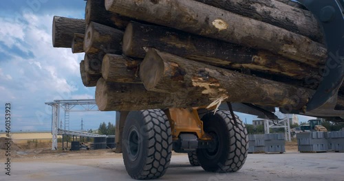 In a woodworking factory, a tractor loader uses a grab to transport a large heap of logs to the loading conveyor 
