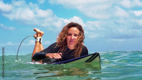 Video footage of surfer girl on white surf board in blue ocean pictured from the water in Bali