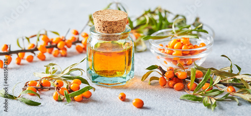 Glass bottle with sea buckthorn oil, berries and branches of sea buckthorn on light background photo