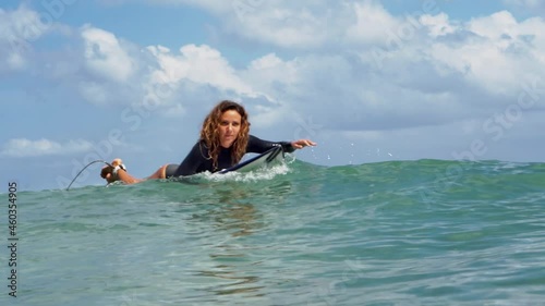 Video footage of surfer girl on white surf board in blue ocean pictured from the water in Bali