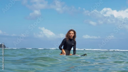 Video footage of surfer girl on white surf board in blue ocean pictured from the water in Bali