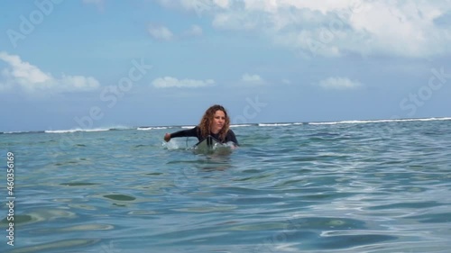 Video footage of surfer girl on white surf board in blue ocean pictured from the water in Bali