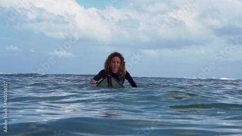 Video footage of surfer girl on white surf board in blue ocean pictured from the water in Bali